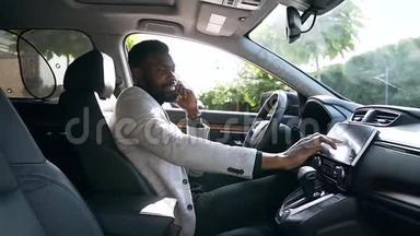 一位时尚、活泼的非裔美国商人坐在司机`座位上，打着电话，调着车